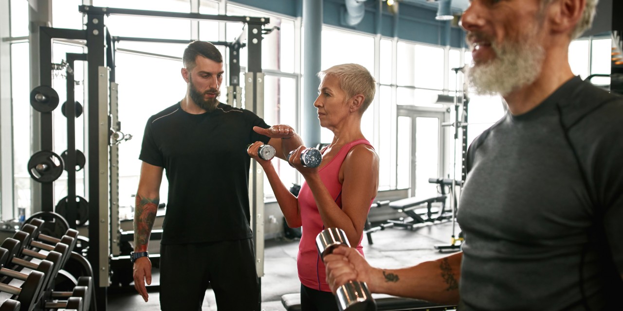 Trening siłowy na siłowni – grupa osób ćwiczących z hantlami pod okiem trenera